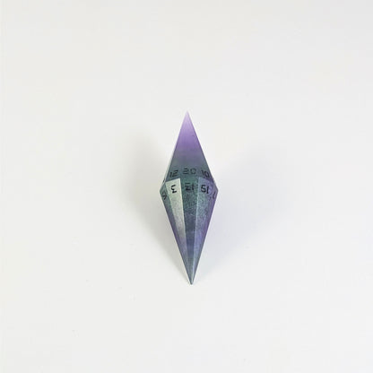 A mid angle view of a diamond d20 with swirls of purple and green with black numbers that glow in the dark on a white background.
