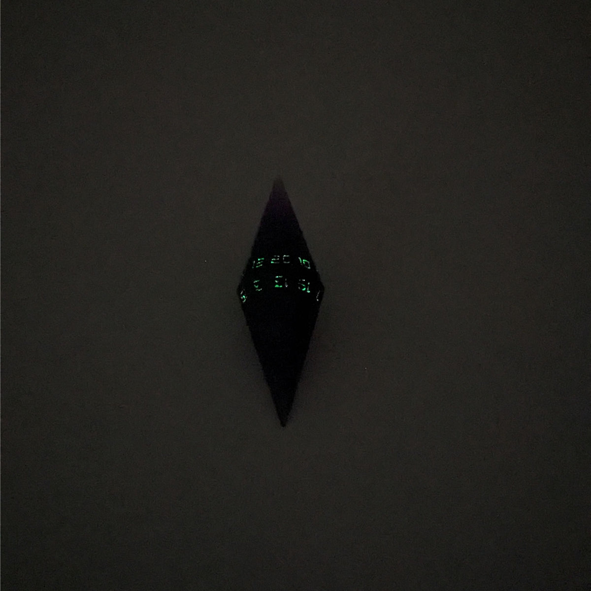 A mid angle view of a diamond d20 with swirls of purple and green with black numbers that glow in the dark on a white background. This photo was taken in the dark to show the black numbers glowing green in the dark.