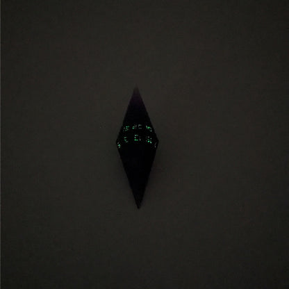 A mid angle view of a diamond d20 with swirls of purple and green with black numbers that glow in the dark on a white background. This photo was taken in the dark to show the black numbers glowing green in the dark.