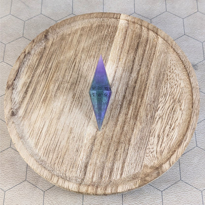 A high angle view of a diamond d20 with swirls of purple and green with black numbers that glow in the dark. It is sitting in the center of a wooden circle.