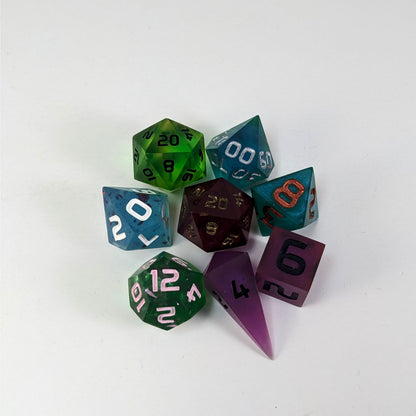 A complete set of 8 handmade artisan dice that are a mismatched array of colors and designs. The DnD dice set is arranged in a circle and features 2 D20s, one of which is in the center surrounded by the other 7 dice.
