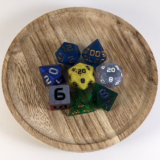 A complete set of 8 handmade artisan dice that are a mismatched array of different colors and designs. The DnD dice set is on a wooden circle and the dice are arranged in a circle and features 2 D20s, one of which is in the center surrounded by the other 7 dice.
