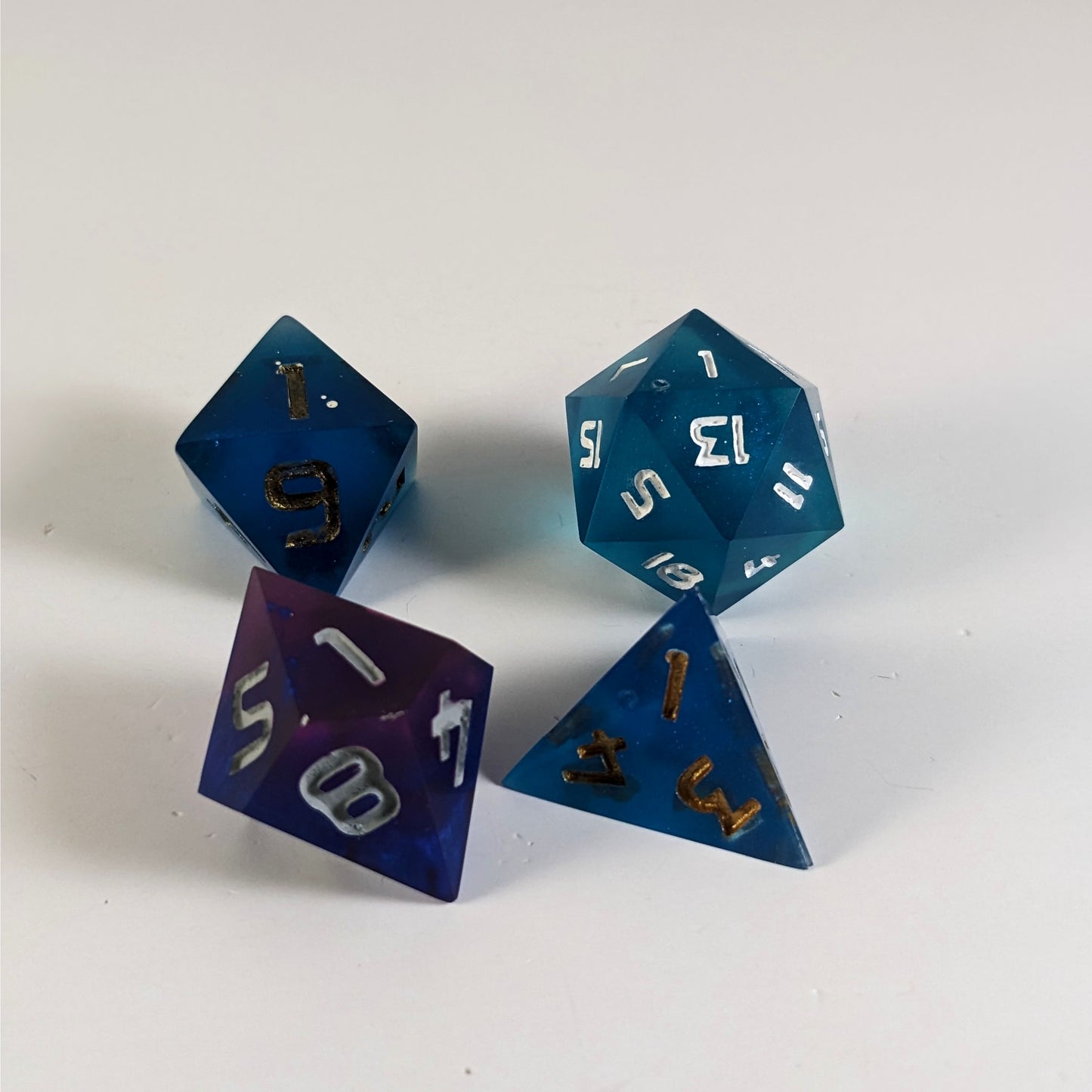 A d20, d8, d10, and d4 are angled to show their cosmetic flaws. Each die has a small bubble or scuff that makes the die imperfect, but would not affect the actual rolling of the die.