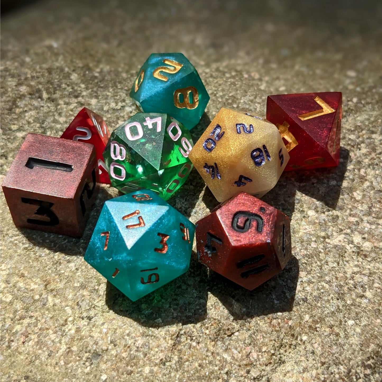 A set of polyhedral dnd dice that are a mismatched array of colors and designs sit on a large rock.