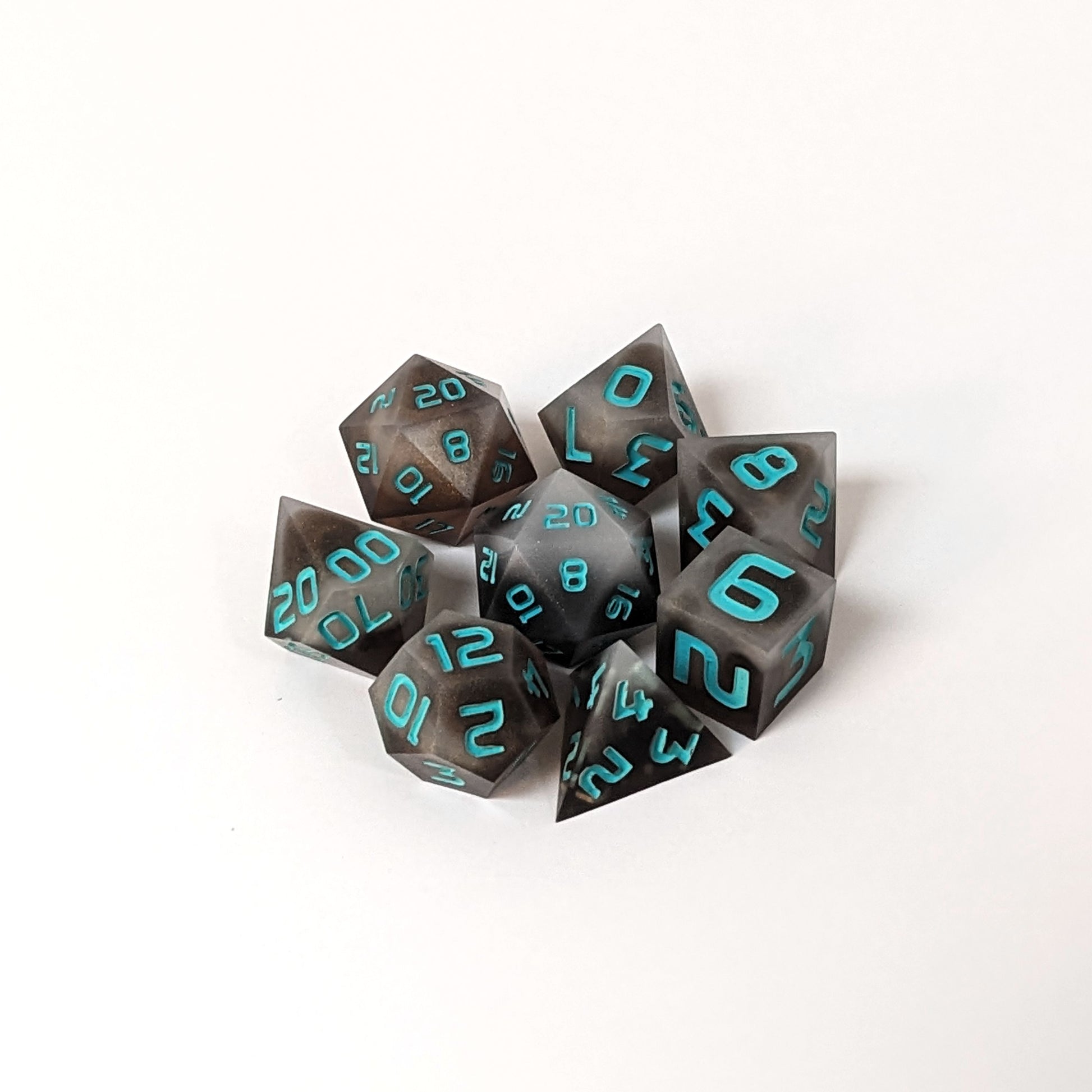 A complete set of 8 handmade artisan dice that are coffee brown with milky white swirls and teal numbers. The DnD dice set is arranged in a circle and features 2 D20s, one of which is in the center surrounded by the other 7 dice on a white background.