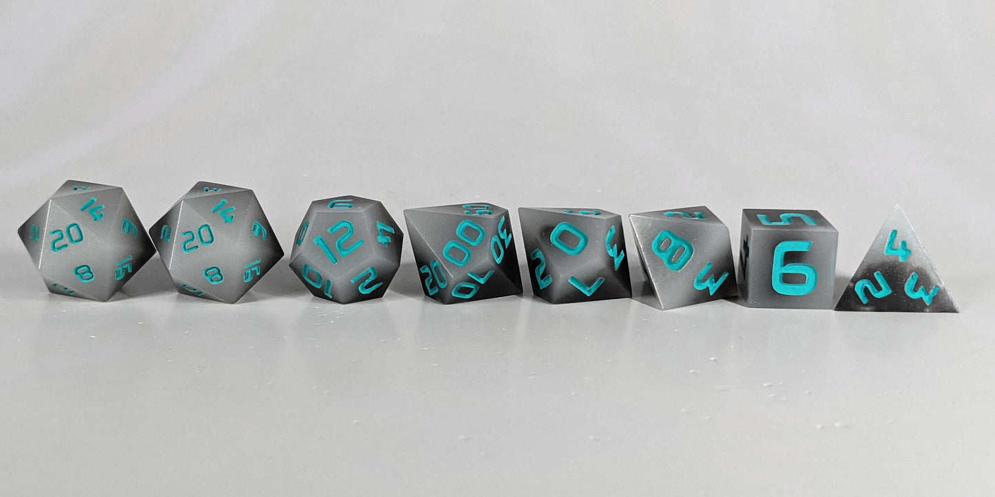 A straight on photo of a complete set of polyhedral dice that are coffee brown with milky white swirls and teal numbers arranged in a straight line. They are lined up with the 2 d20s on the left going down to the d4 on the right side. The highest value number of each die is facing forward