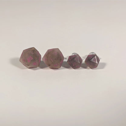 Two pairs of handmade d20 earrings with titanium hardware that are brown and white swirled with pink numbers on a white background sit in a line with the larger pair on the left and the smaller pair on the right. The earrings on the left of each pair centers the 20 face and the earrings on the right of each pair centers the 1 face.