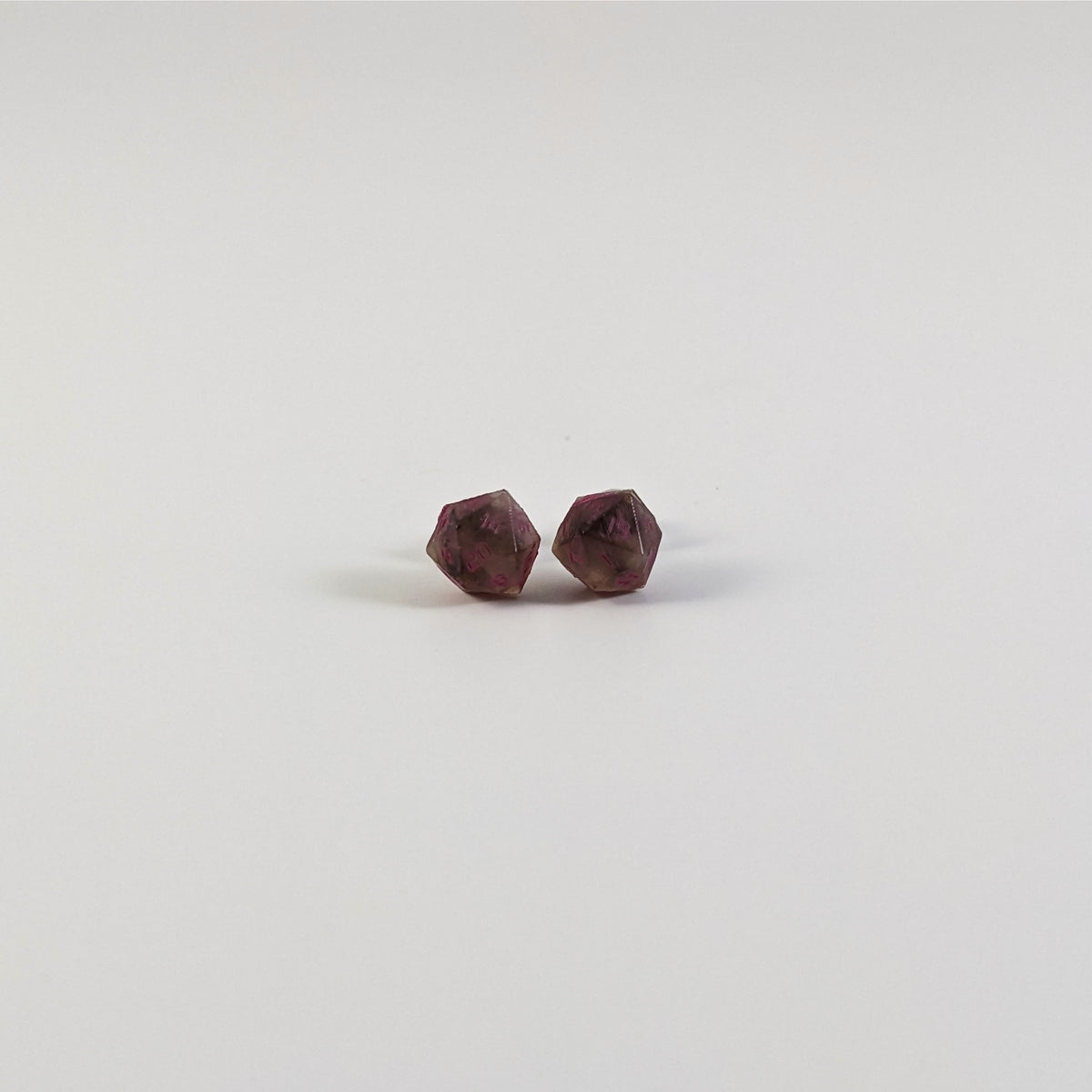 A single pair of the smaller size handmade d20 earrings with titanium hardware that are brown and white swirled with pink numbers on a white background. The earring on the left centers the 20 face and the earring on the right centers the 1 face.