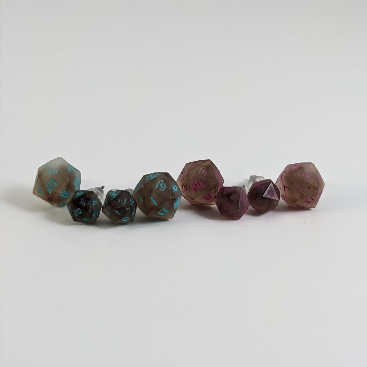Four pairs of brown and white d20 stud earrings with titanium hardware on a white background. There are 2 large pairs and 2 small pairs, and one pair of each of those has teal numbers and pink numbers.