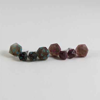 Four pairs of brown and white d20 stud earrings with titanium hardware on a white background. There are 2 large pairs and 2 small pairs, and one pair of each of those has teal numbers and pink numbers.