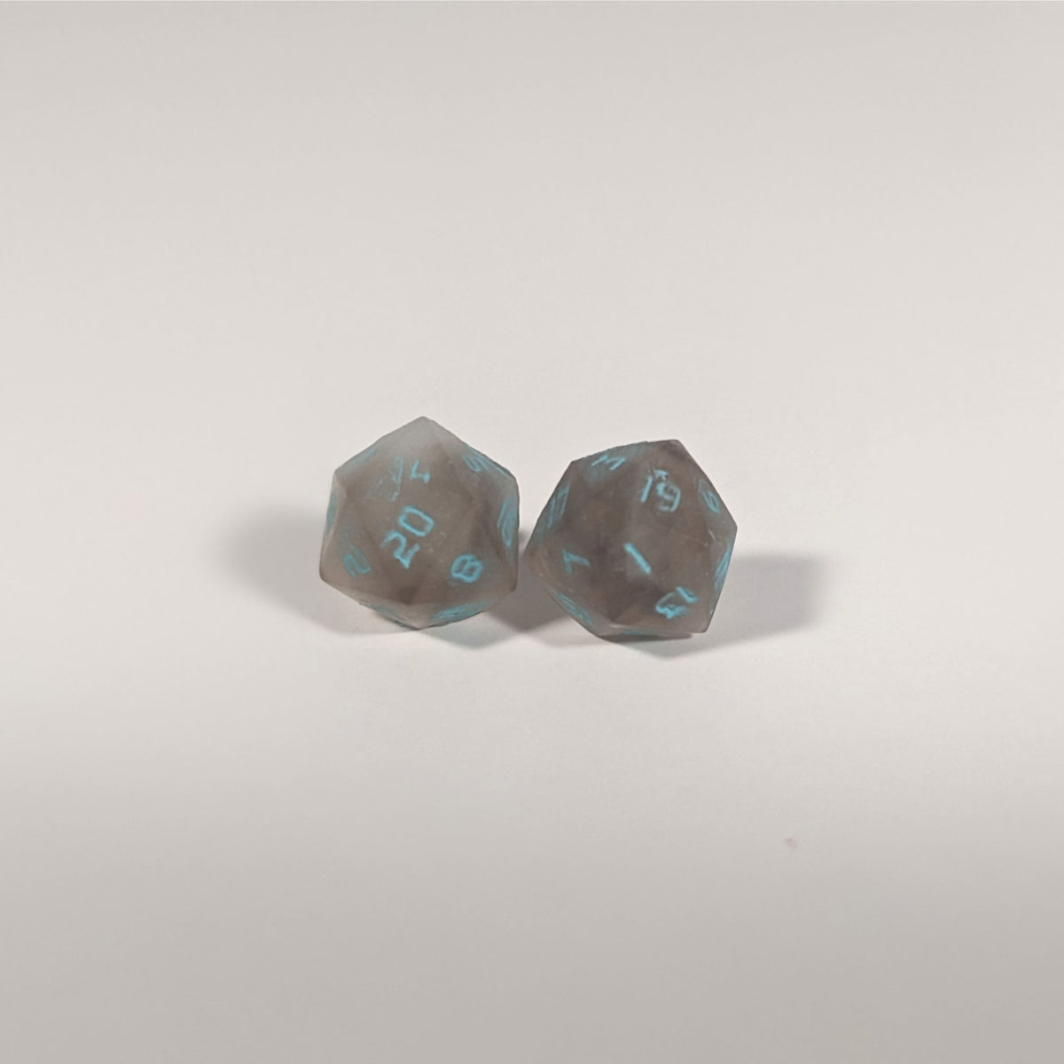 A single pair of the larger size handmade d20 earrings with titanium hardware that are brown and white swirled with teal numbers on a white background. The earring on the left centers the 20 face and the earring on the right centers the 1 face.
