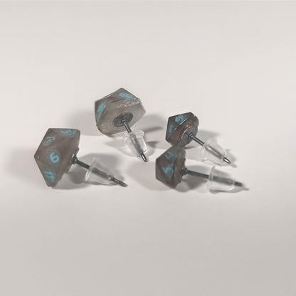 Two pairs of handmade d20 earrings that are brown and white swirled with teal numbers turned to show the titanium hardware and bell shaped rubber backs.
