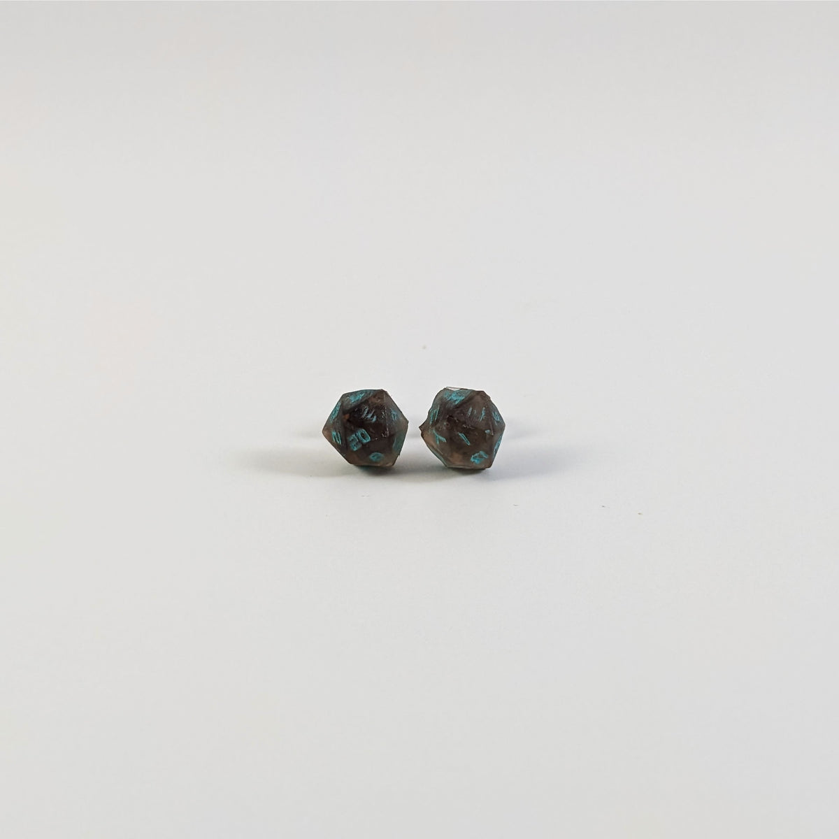 A single pair of the smaller size handmade d20 earrings with titanium hardware that are brown and white swirled with teal numbers on a white background. The earring on the left centers the 20 face and the earring on the right centers the 1 face.