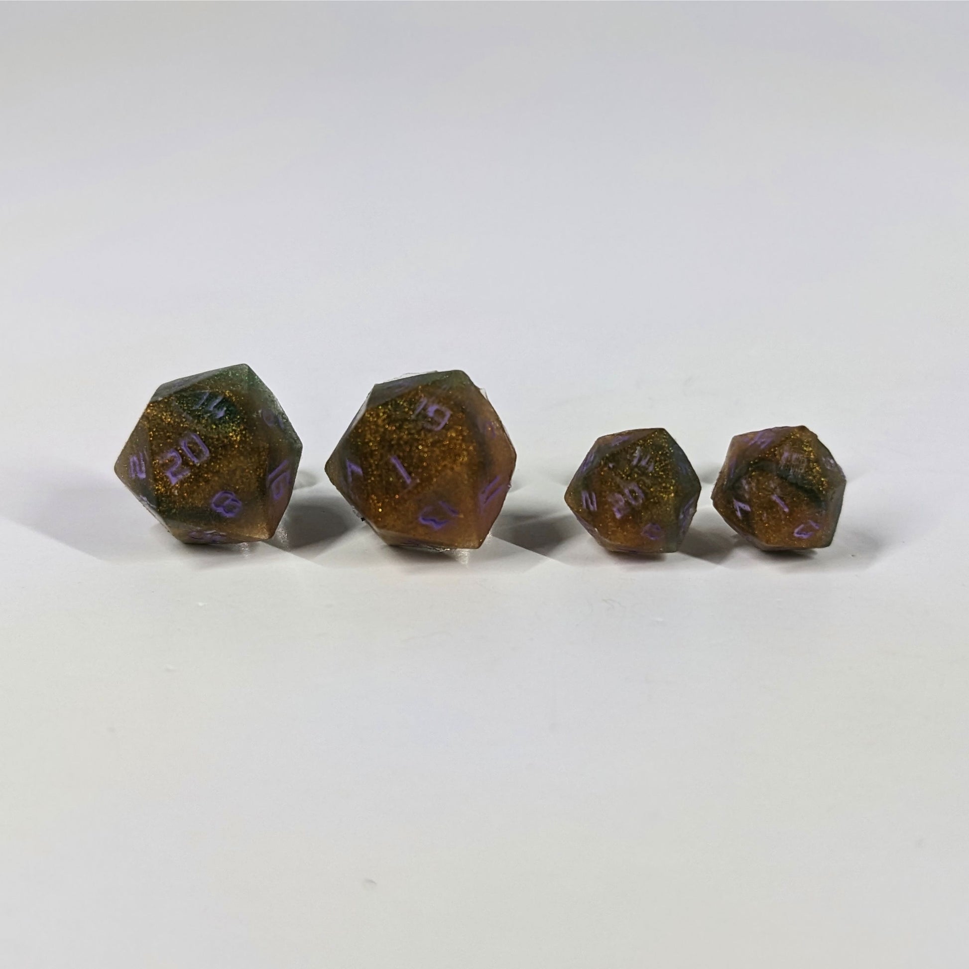 Two pairs of handmade d20 earrings with sterling silver hardware that are dark green and red gold with purple numbers on a white background sit in a line with the larger pair on the left and the smaller pair on the right. The earrings on the left of each pair centers the 20 face and the earrings on the right of each pair centers the 1 face.