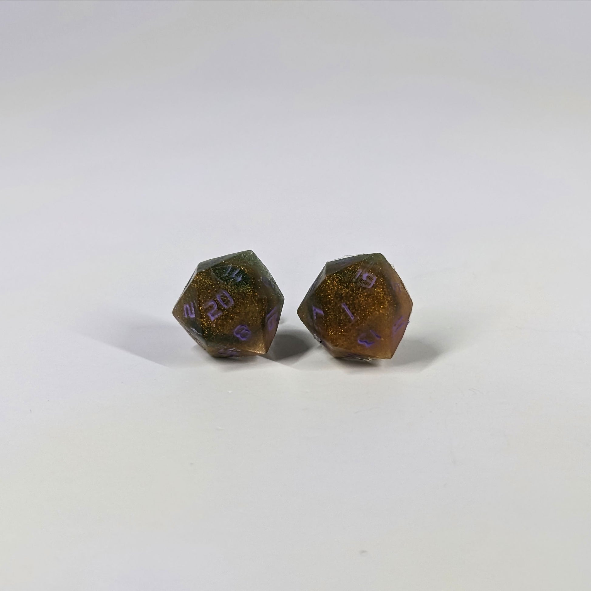 A single pair of the larger size handmade d20 earrings with sterling silver hardware that are dark green and red gold with purple numbers on a white background. The earring on the left centers the 20 face and the earring on the right centers the 1 face.