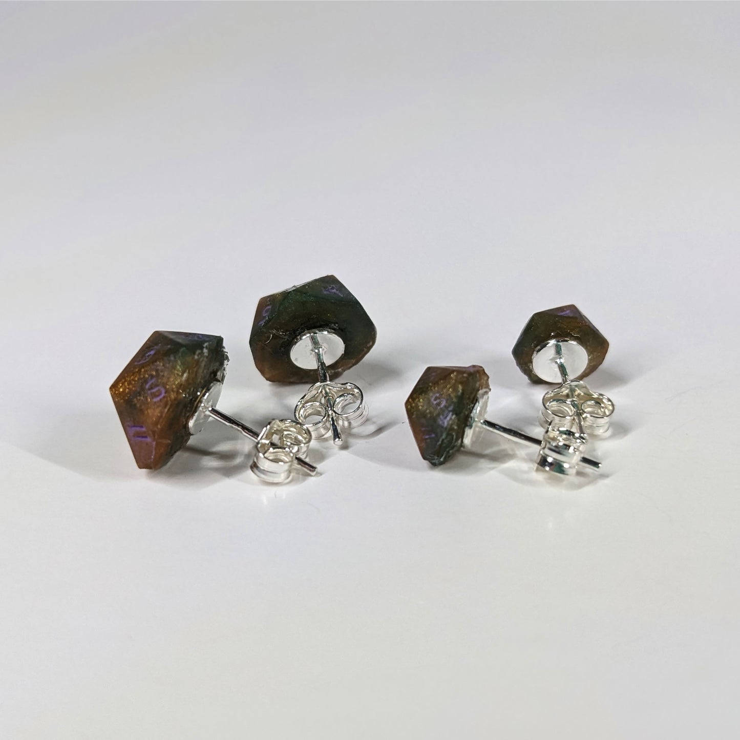 Two pairs of handmade d20 earrings that are dark green and red gold with purple numbers turned to show the sterling silver hardware and butterfly backs.