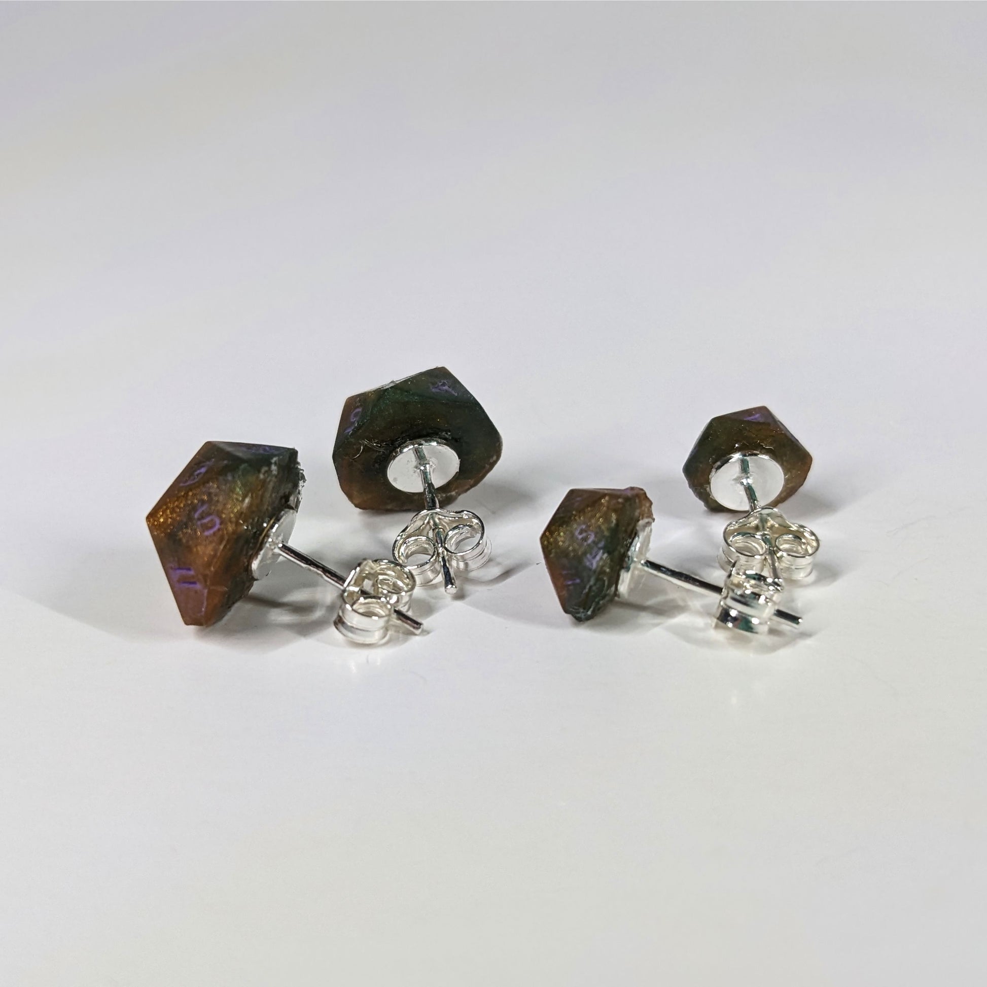Two pairs of handmade d20 earrings that are dark green and red gold with purple numbers turned to show the sterling silver hardware and butterfly backs.