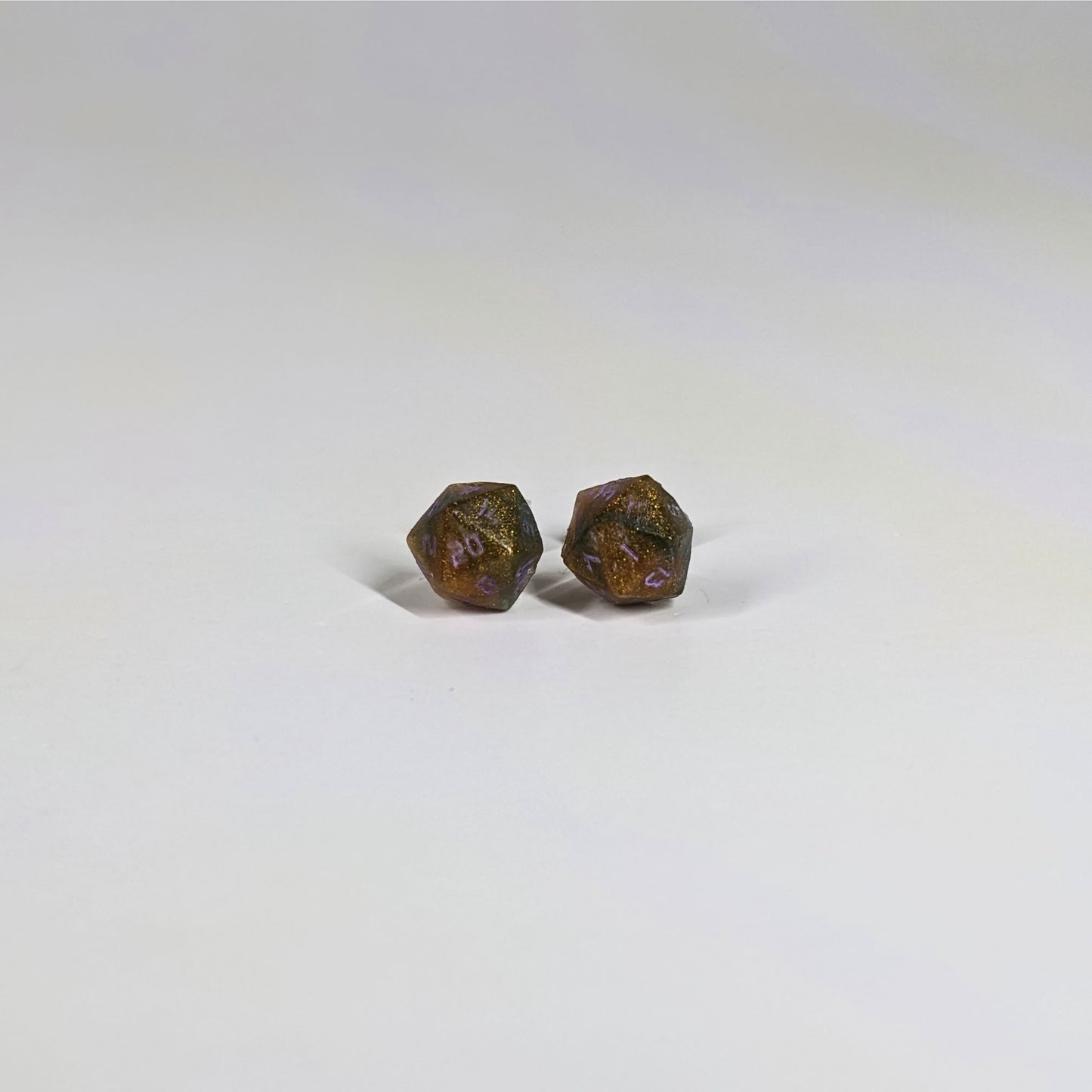 A single pair of the smaller size handmade d20 earrings with sterling silver hardware that are dark green and red gold with purple numbers on a white background. The earring on the left centers the 20 face and the earring on the right centers the 1 face.