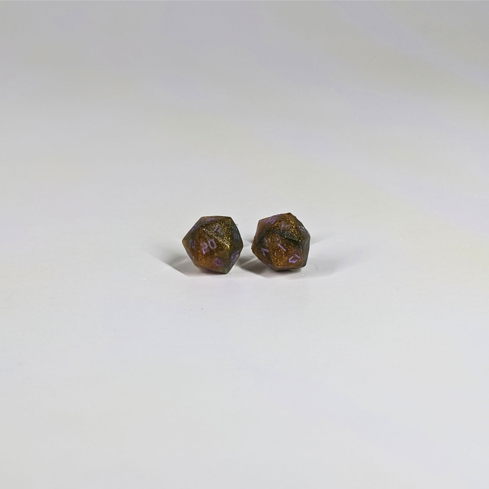 A single pair of the smaller size handmade d20 earrings with sterling silver hardware that are dark green and red gold with purple numbers on a white background. The earring on the left centers the 20 face and the earring on the right centers the 1 face.