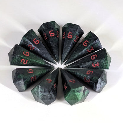 Ten dagger shaped d6s are arranged in a circle with all the points of the dice pointing in towards a central point on a white background. The dice are black and dark green with red numbers, and the face up numbers are all 6.