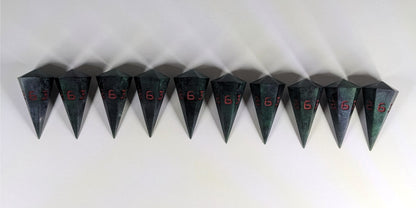 Ten dagger shaped d6s are arranged in a line with the points of the dice facing downwards. The dice are dark green and black with red numbers, and they all have the 6 face up.