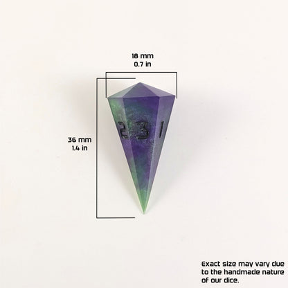 A size graphic of a dagger d3. The die is purple and green with black numbers. The die is 36 mm 1.4 in tall and 18 mm 0.7 in wide. The bottom right corner notes "Exact size may vary due to the handmade nature of our dice."
