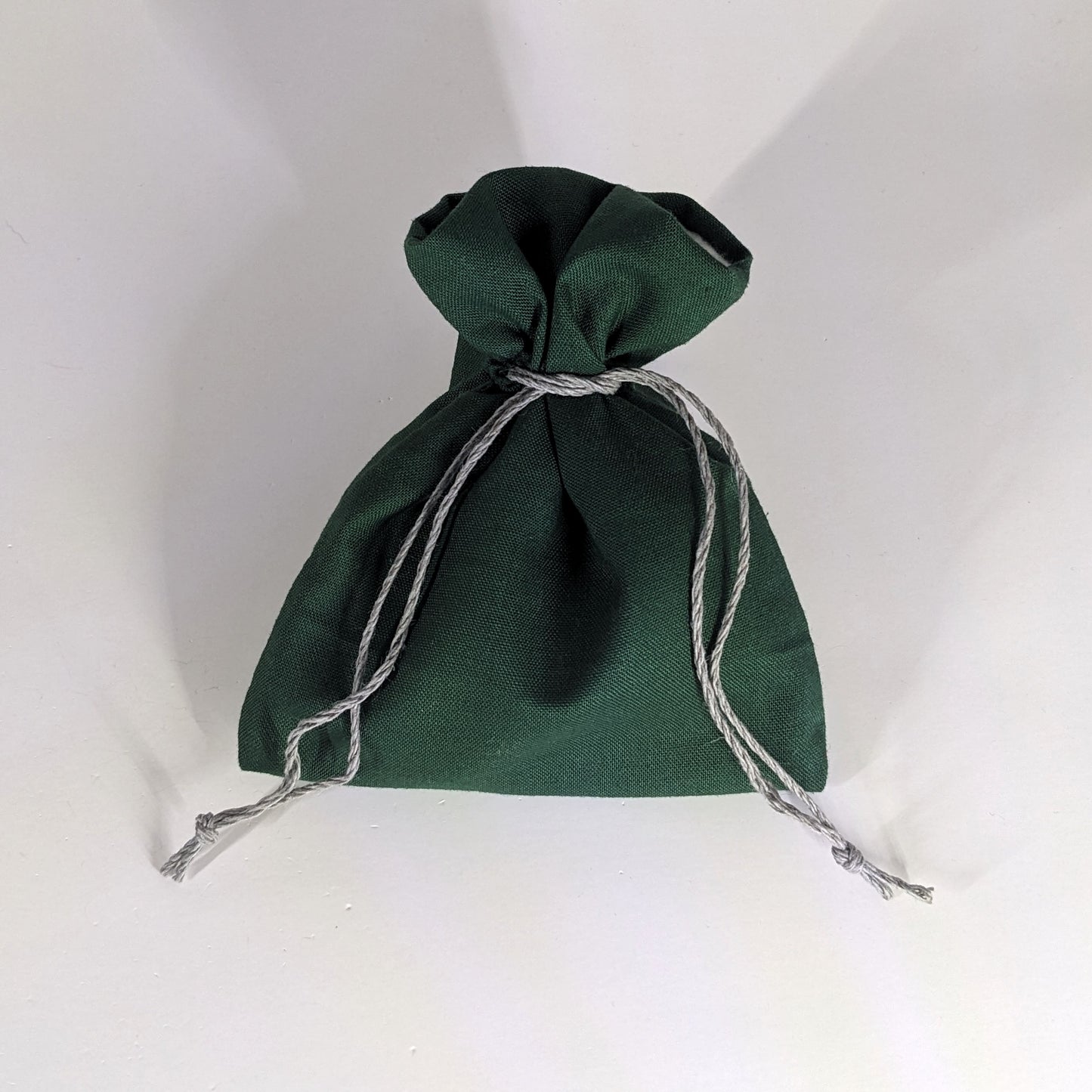 A small, handmade dice bag that is dark green is tied closed on a white background.