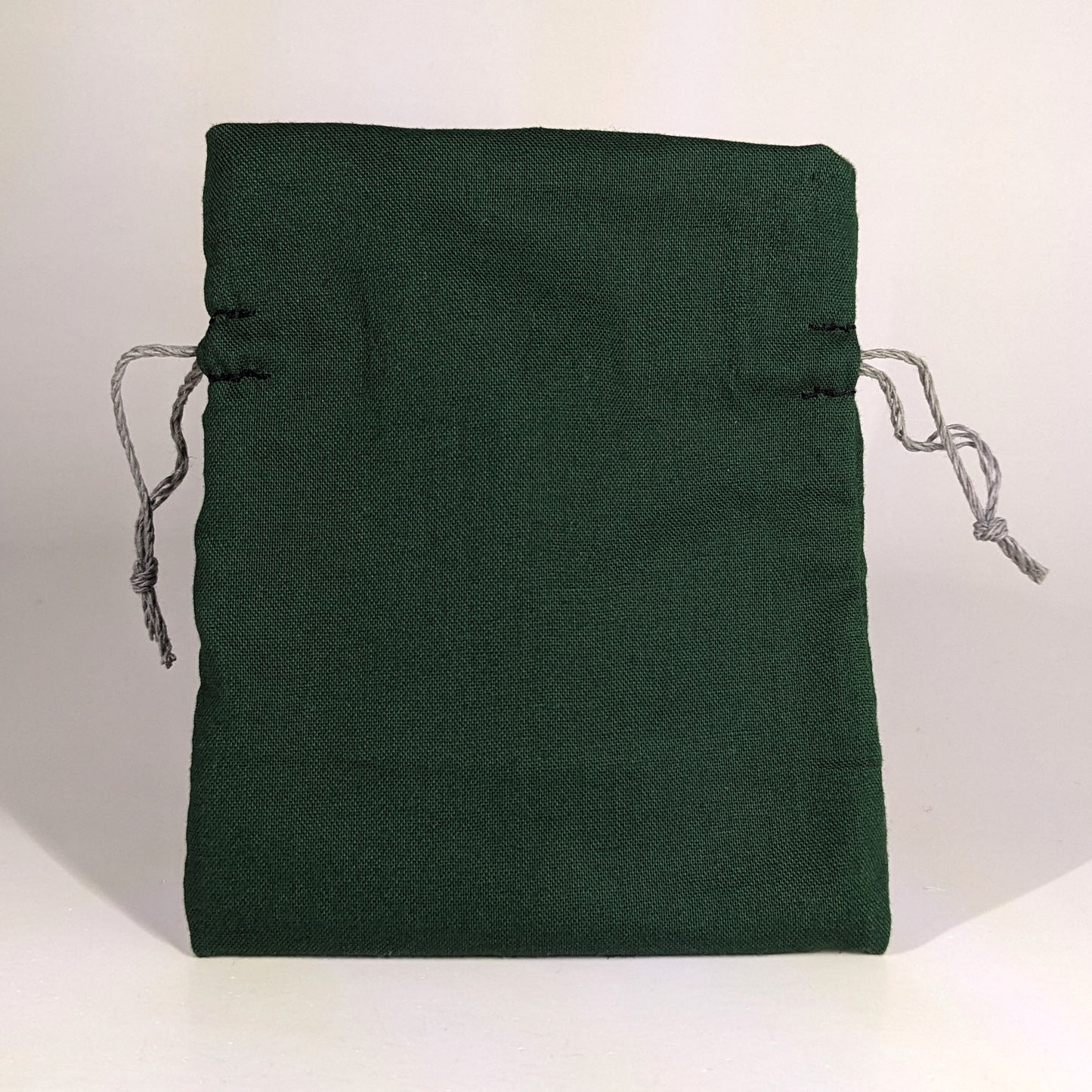 A small, handmade dice bag that is dark green stands upright on a white background.