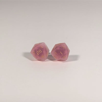 A single pair of the larger size handmade d20 earrings with titanium hardware that are bright pink with gold numbers on a white background. The earring on the left centers the 20 face and the earring on the right centers the 1 face.