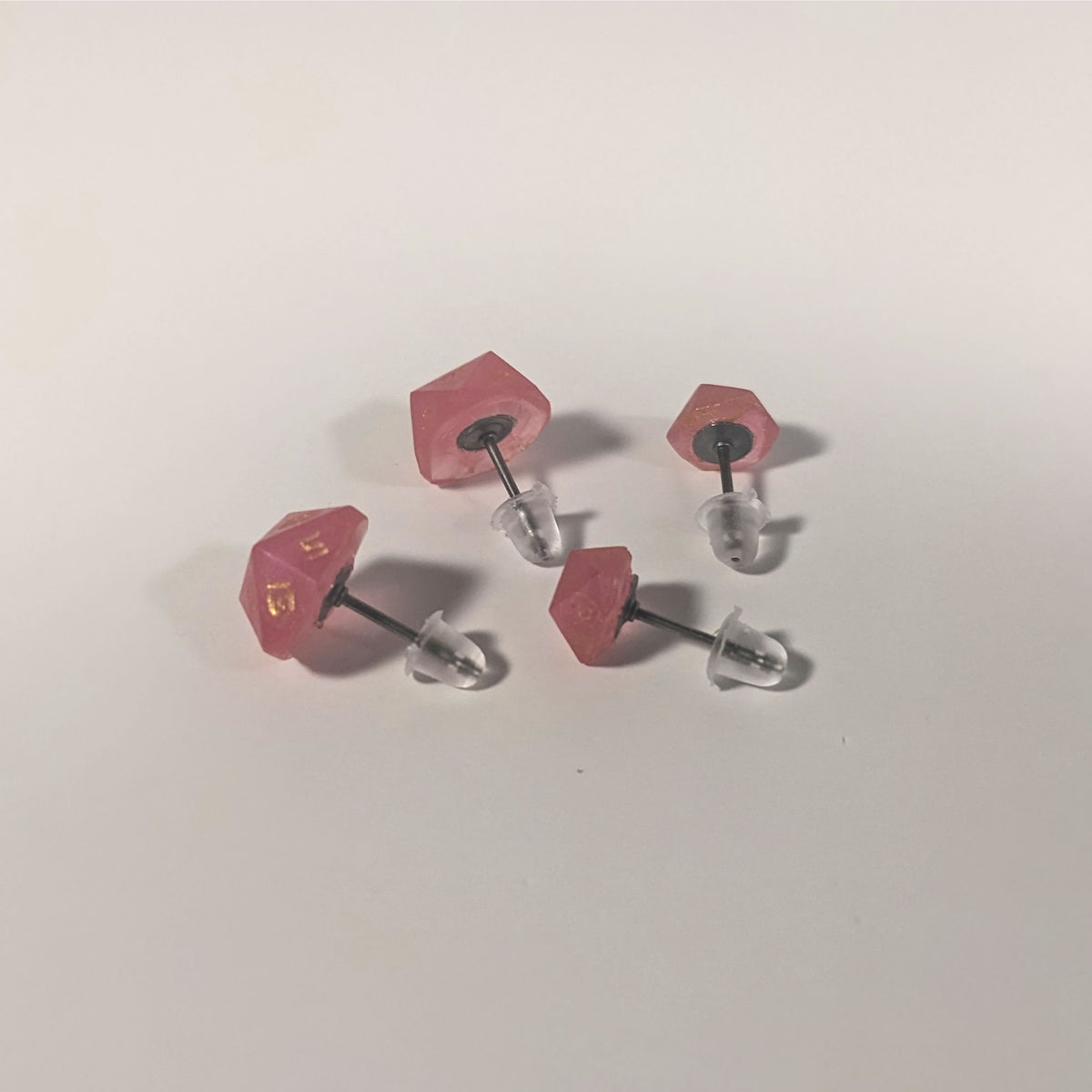 Two pairs of handmade d20 earrings that are bright pink with gold numbers turned to show the titanium hardware and bell shaped rubber backs.