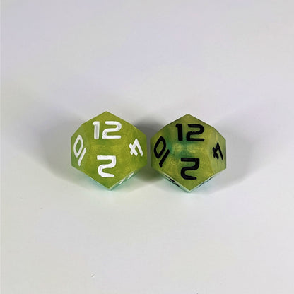Two handmade d12s sit with the 12 faces up on a white background. The dice are yellow and teal. The die on the left has white numbers, the die on the right has black numbers.
