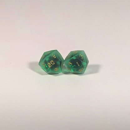 A single pair of the larger size handmade d20 earrings with titanium hardware that are green with black flakies with gold numbers on a white background. The earring on the left centers the 20 face and the earring on the right centers the 1 face.