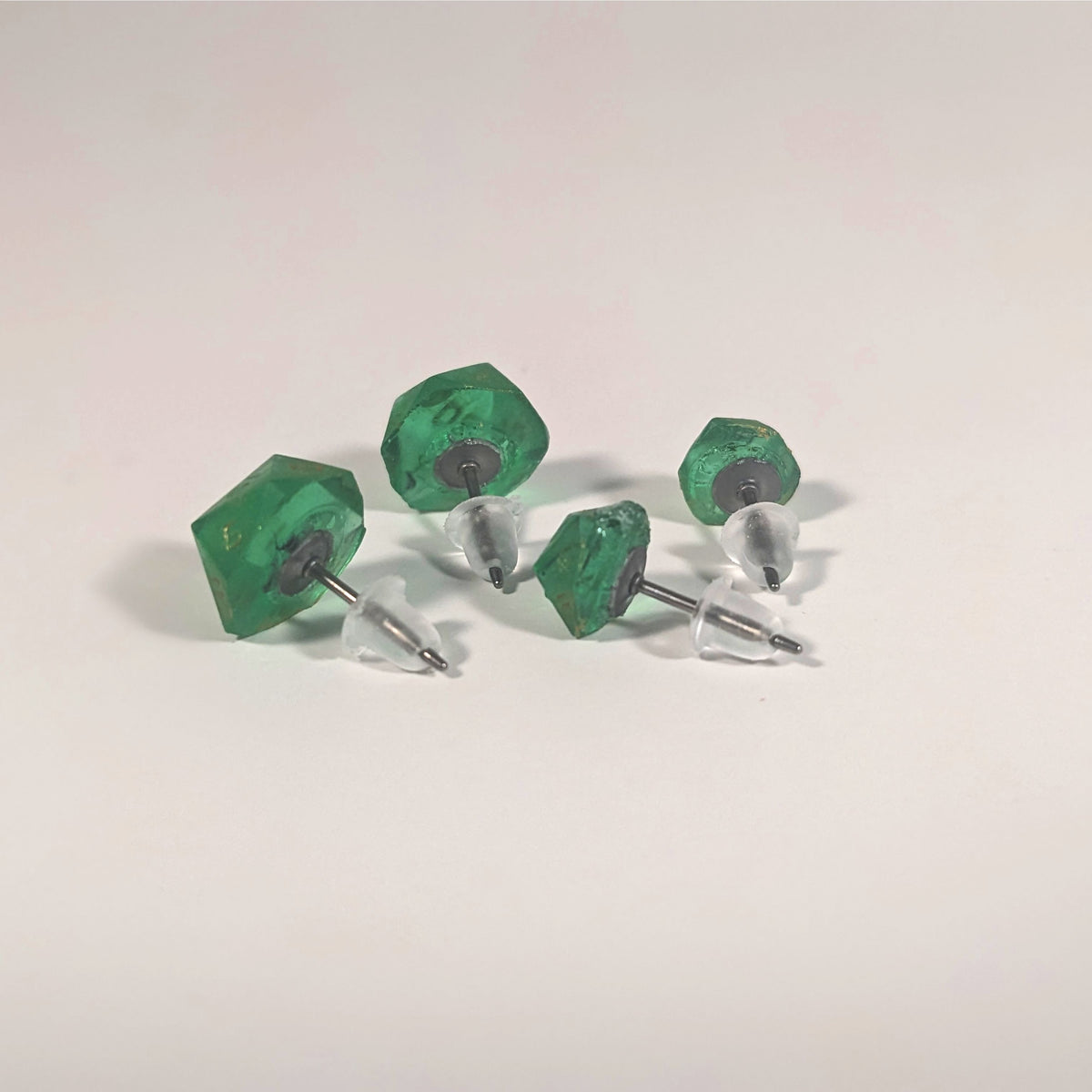 Two pairs of handmade d20 earrings that are green with black flakies with gold numbers turned to show the titanium hardware and bell shaped rubber backs.