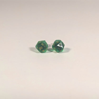 A single pair of the smaller size handmade d20 earrings with titanium hardware that are green with black flakies with gold numbers on a white background. The earring on the left centers the 20 face and the earring on the right centers the 1 face.