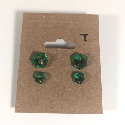 Two pairs of handmade d20 earrings with titanium hardware that are green with black flakies with gold numbers on a kraft brown earring card with a T in the top right corner. The earrings on the left of each pair centers the 20 face and the earrings on the right of each pair centers the 1 face.
