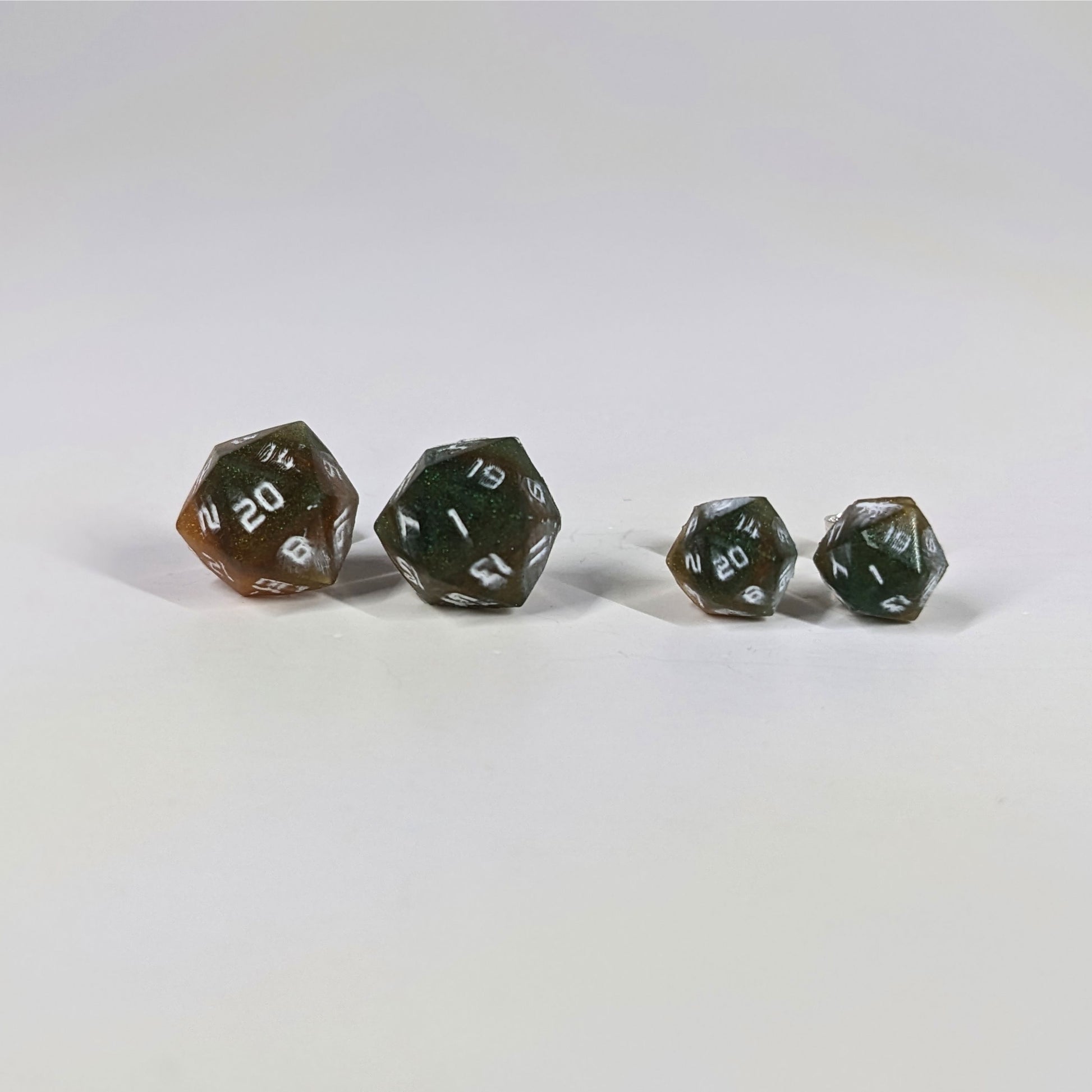 Two pairs of handmade d20 earrings with sterling silver hardware that are dark green and red gold with white numbers on a white background sit in a line with the larger pair on the left and the smaller pair on the right. The earrings on the left of each pair centers the 20 face and the earrings on the right of each pair centers the 1 face.