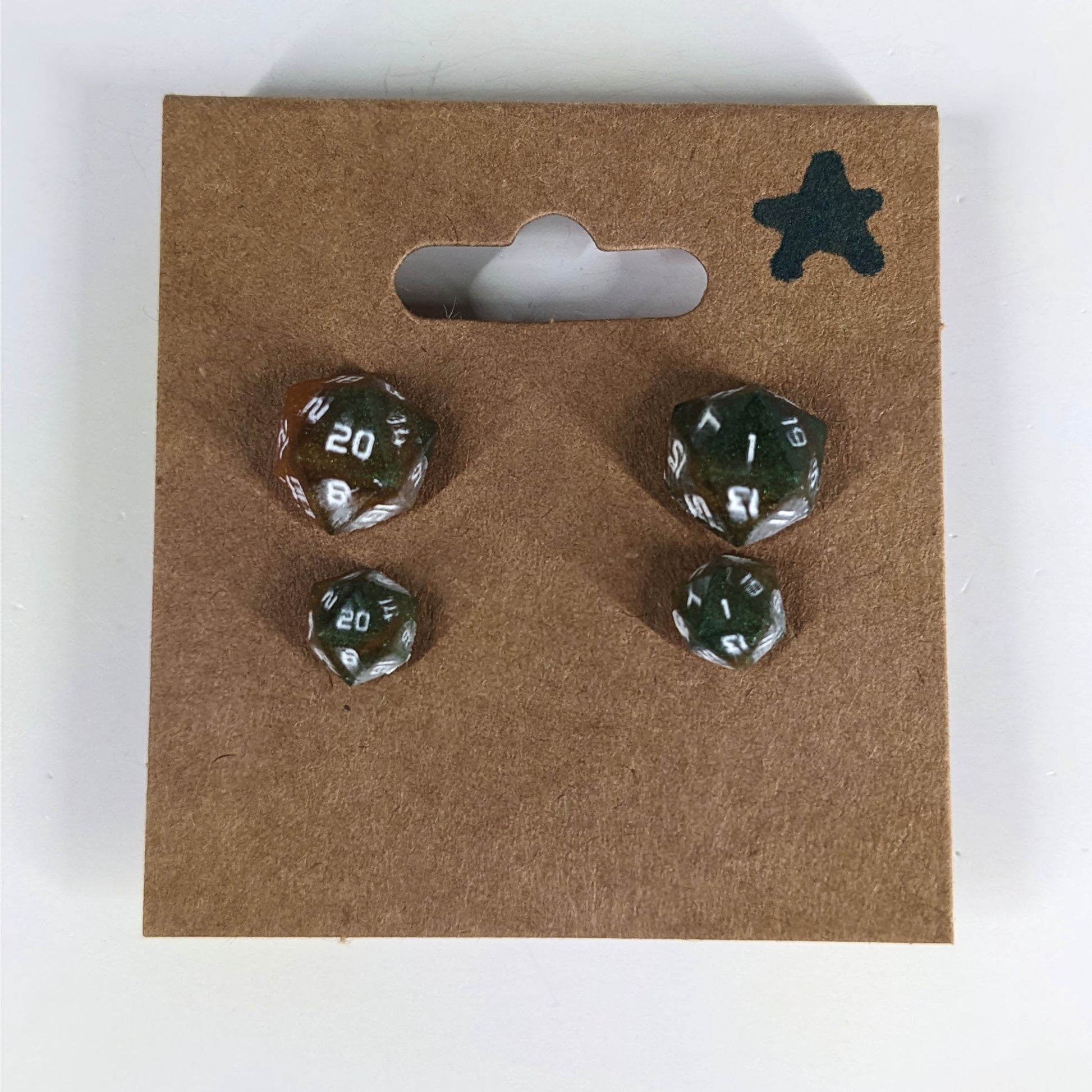 Two pairs of handmade d20 earrings with sterling silver hardware that are dark green and red gold with white numbers on a kraft brown earring card with a star in the top right corner. The earrings on the left of each pair centers the 20 face and the earrings on the right of each pair centers the 1 face.