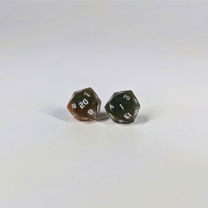 A single pair of the larger size handmade d20 earrings with sterling silver hardware that are dark green and red gold with white numbers on a white background. The earring on the left centers the 20 face and the earring on the right centers the 1 face.