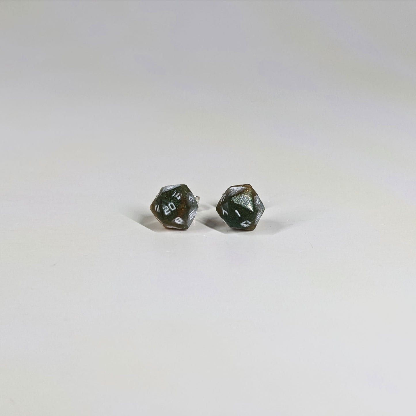 A single pair of the smaller size handmade d20 earrings with sterling silver hardware that are dark green and red gold with white numbers on a white background. The earring on the left centers the 20 face and the earring on the right centers the 1 face.
