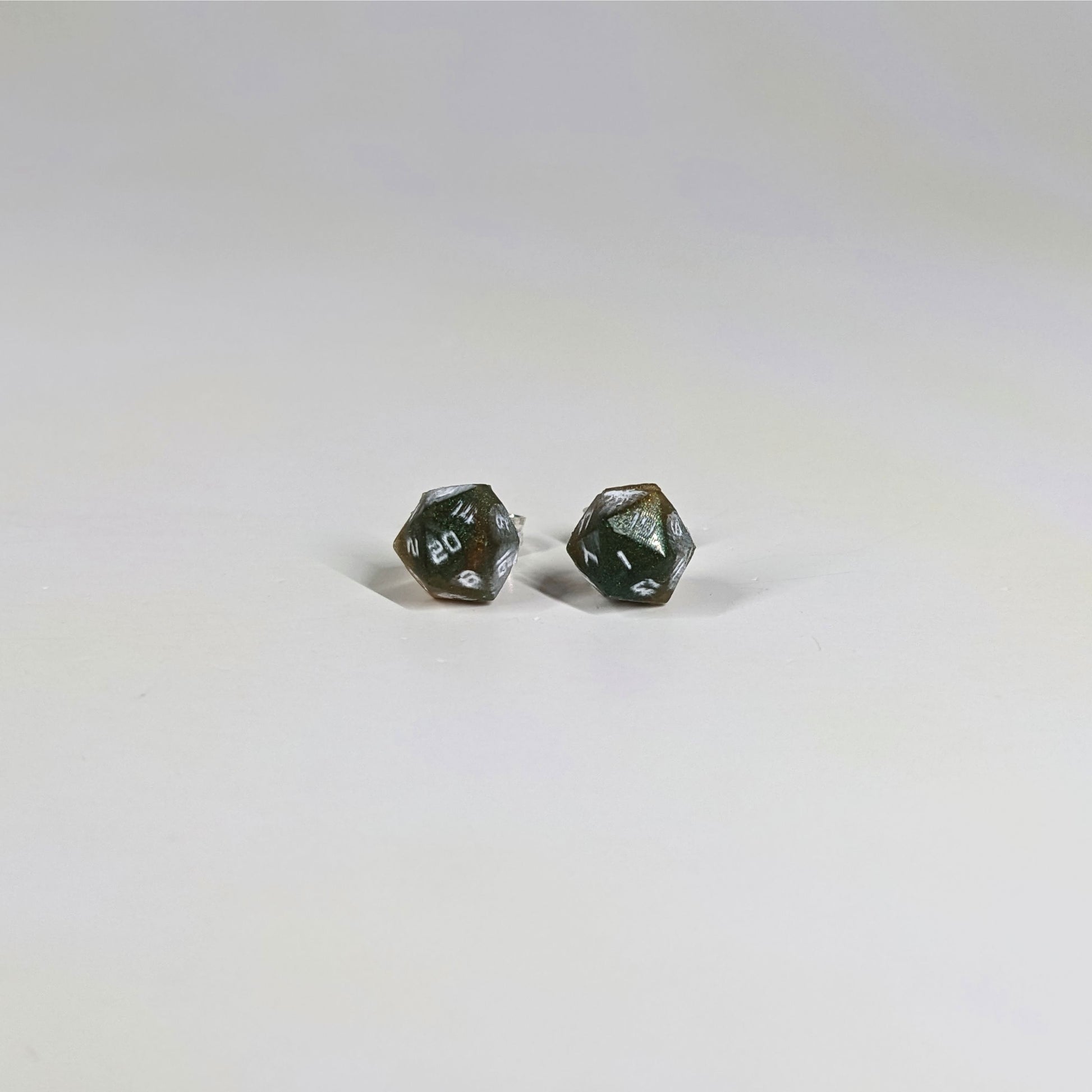 A single pair of the smaller size handmade d20 earrings with sterling silver hardware that are dark green and red gold with white numbers on a white background. The earring on the left centers the 20 face and the earring on the right centers the 1 face.