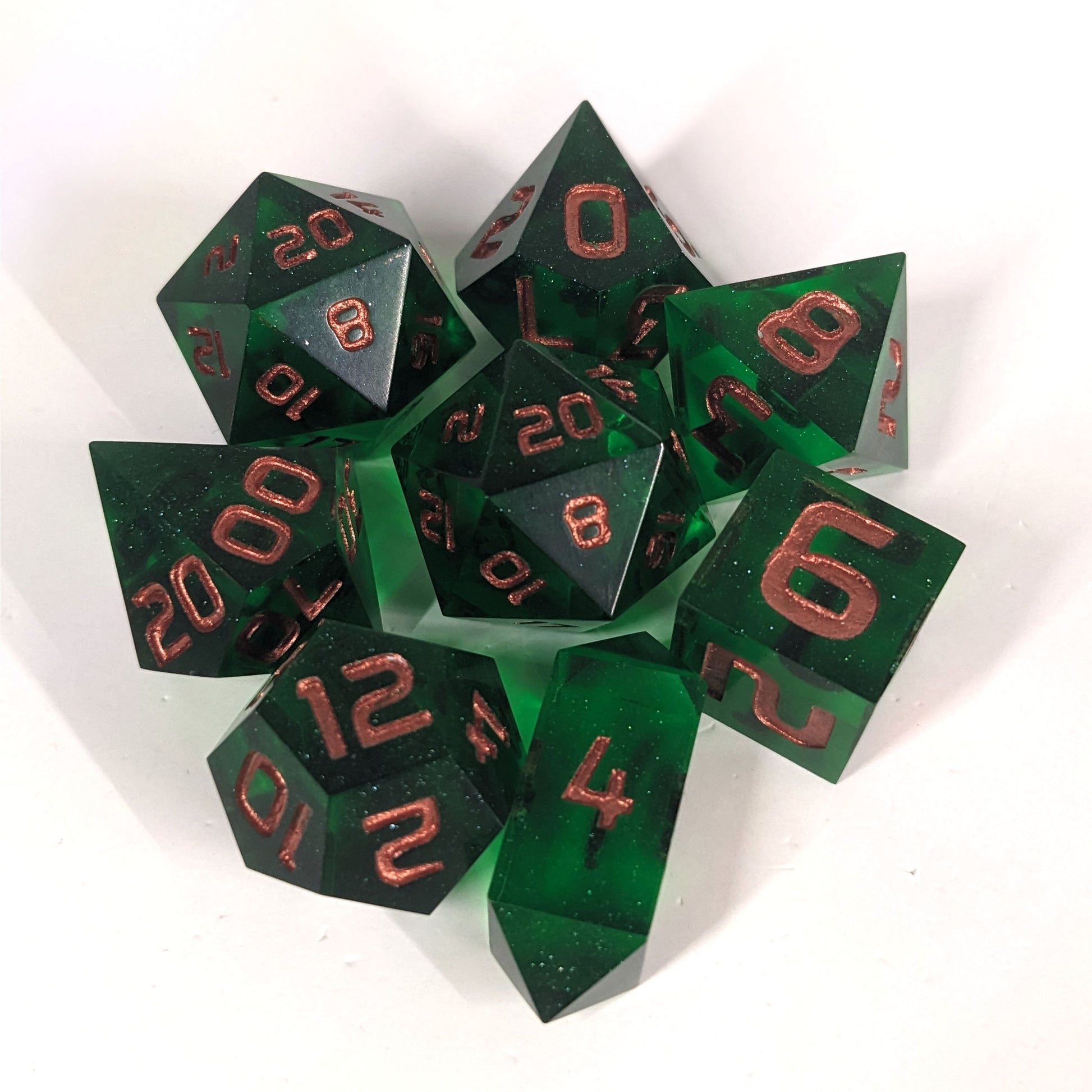 A complete set of 8 handmade artisan dice that are emerald green with copper numbers. The DnD dice set is arranged in a circle and features 2 D20s, one of which is in the center surrounded by the other 7 dice on a white background. The d4 is a unique, crystalline shape.