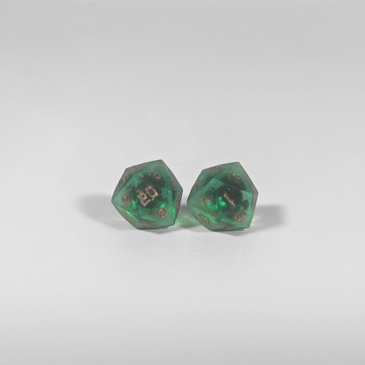 A single pair of the larger size handmade d20 earrings with titanium hardware that are emerald green with copper numbers on a white background. The earring on the left centers the 20 face and the earring on the right centers the 1 face.
