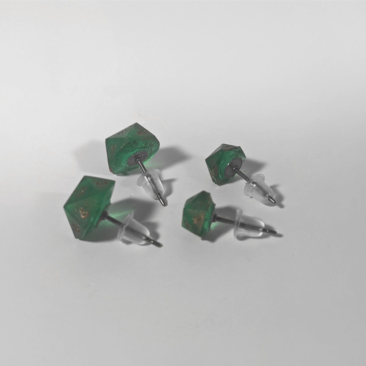 Two pairs of handmade d20 earrings that are emerald green with copper numbers turned to show the titanium hardware and bell shaped rubber backs.