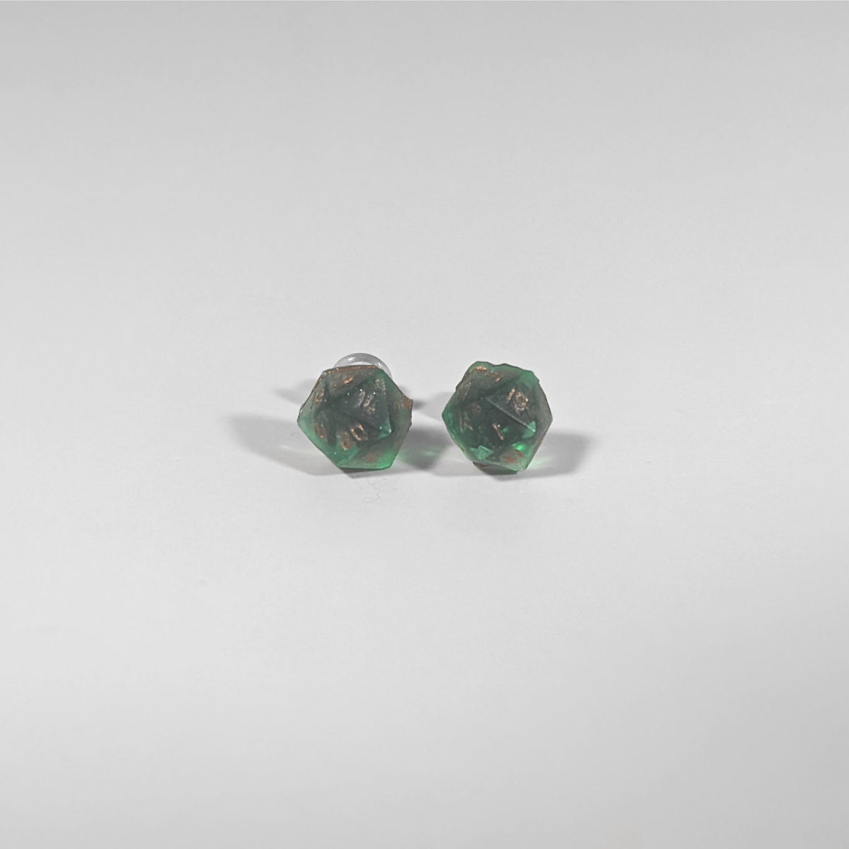 A single pair of the smaller size handmade d20 earrings with titanium hardware that are emerald green with copper numbers on a white background. The earring on the left centers the 20 face and the earring on the right centers the 1 face.