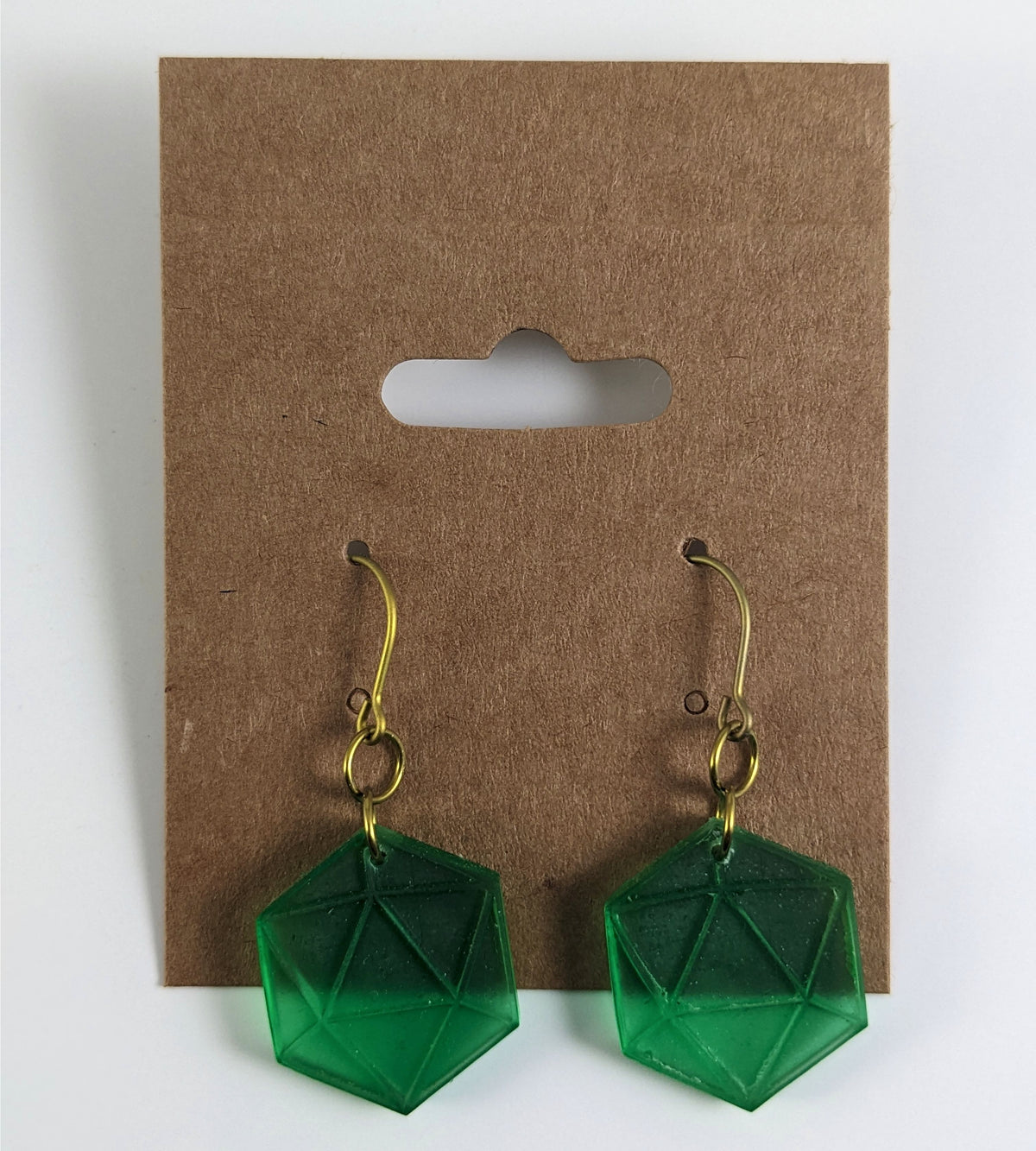 A pair of emerald green dangly, flat d20 earrings with gold color titanium and niobium hardware on a kraft earring card on a white background.