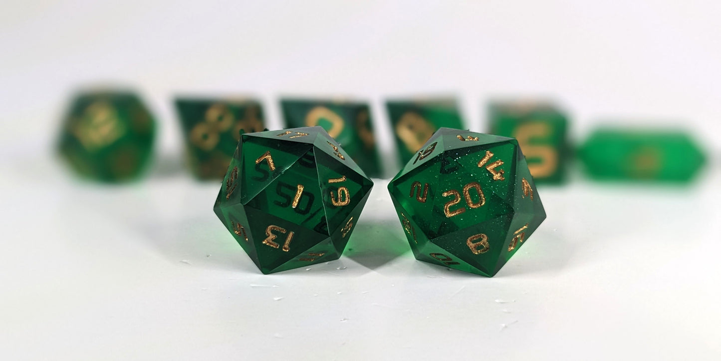 A straight on photo of a standard set of DnD dice that are emerald green with gold numbers focusing on 2 d20s in the center. The d20 on the left has the 1 face centered and the d20 on the right has the 20 face centered. The other 6 dice are lined up in the background but are out of focus, while the d20s are in sharp focus.