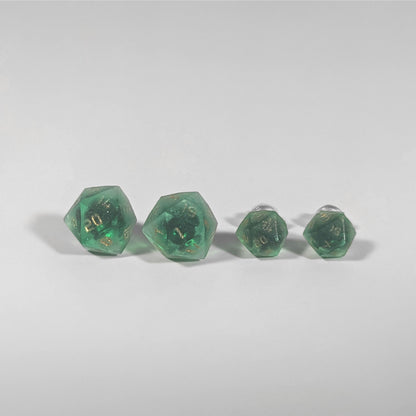 Two pairs of handmade d20 earrings with titanium hardware that are emerald green with gold numbers on a white background sit in a line with the larger pair on the left and the smaller pair on the right. The earrings on the left of each pair centers the 20 face and the earrings on the right of each pair centers the 1 face.