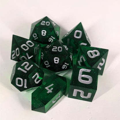 A complete set of 8 handmade artisan dice that are emerald green with silver numbers. The DnD dice set is arranged in a circle and features 2 D20s, one of which is in the center surrounded by the other 7 dice on a white background. The d4 is a unique, crystalline shape.