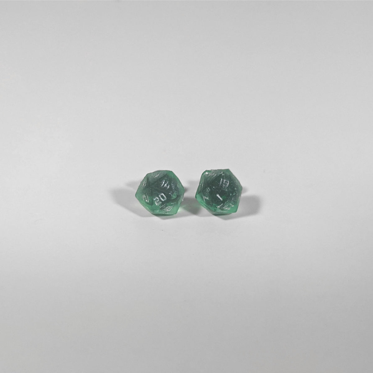 A single pair of the smaller size handmade d20 earrings with titanium hardware that are emerald green with silver numbers on a white background. The earring on the left centers the 20 face and the earring on the right centers the 1 face.