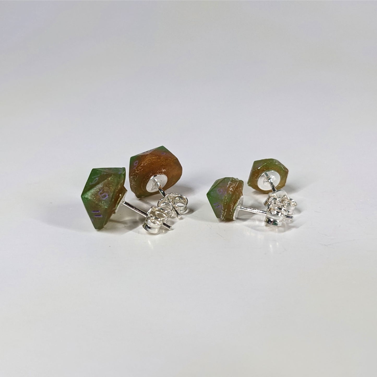 Two pairs of handmade d20 earrings that are bright green and red gold with purple numbers turned to show the sterling silver hardware and butterfly backs.